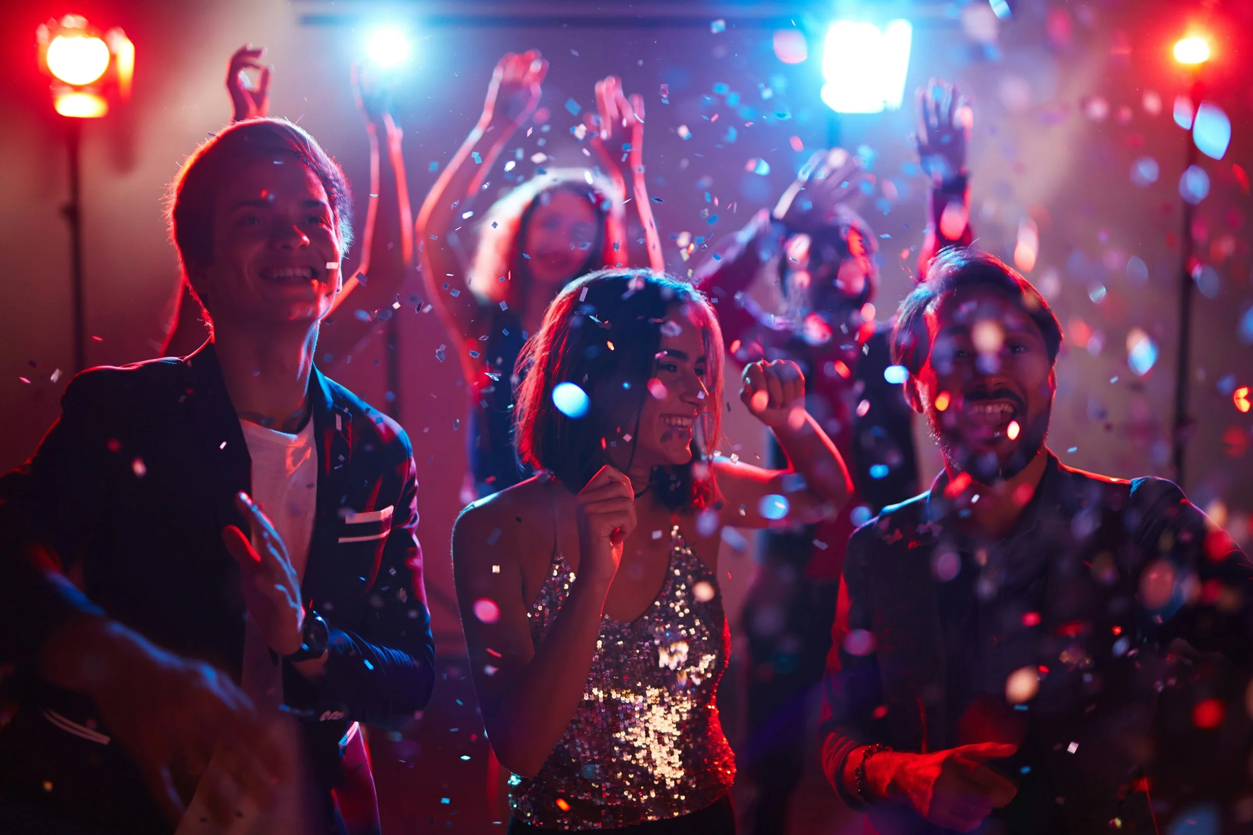 People dancing and celebrating at a party with colorful lights and confetti.