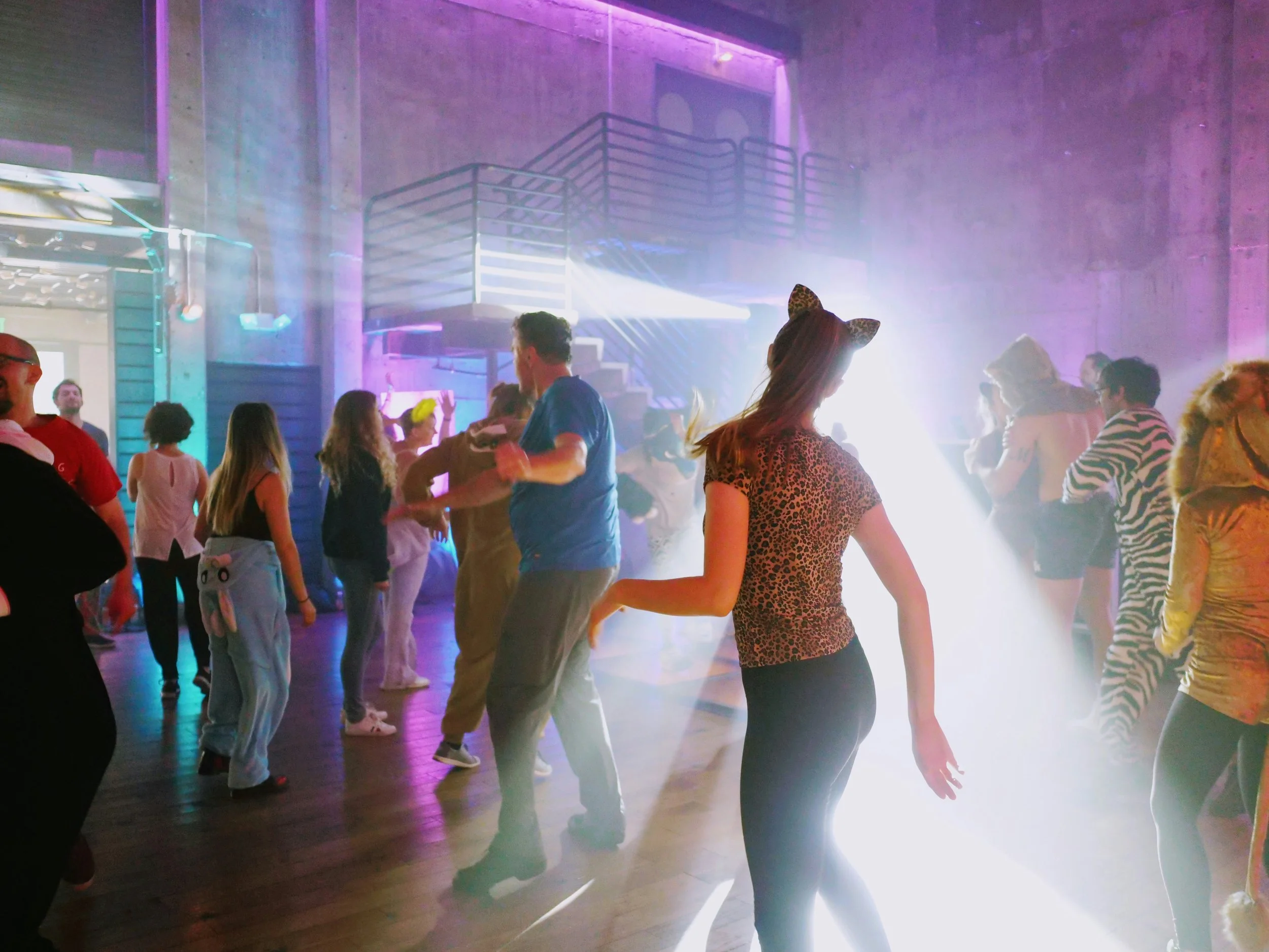 People dancing at a party with colorful lights and fog.