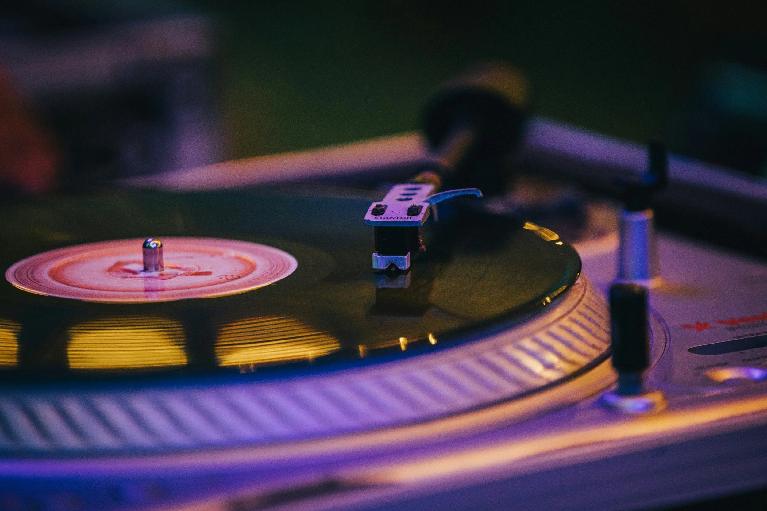 Close-up of a turntable with a record spinning, illuminated by colorful lighting.