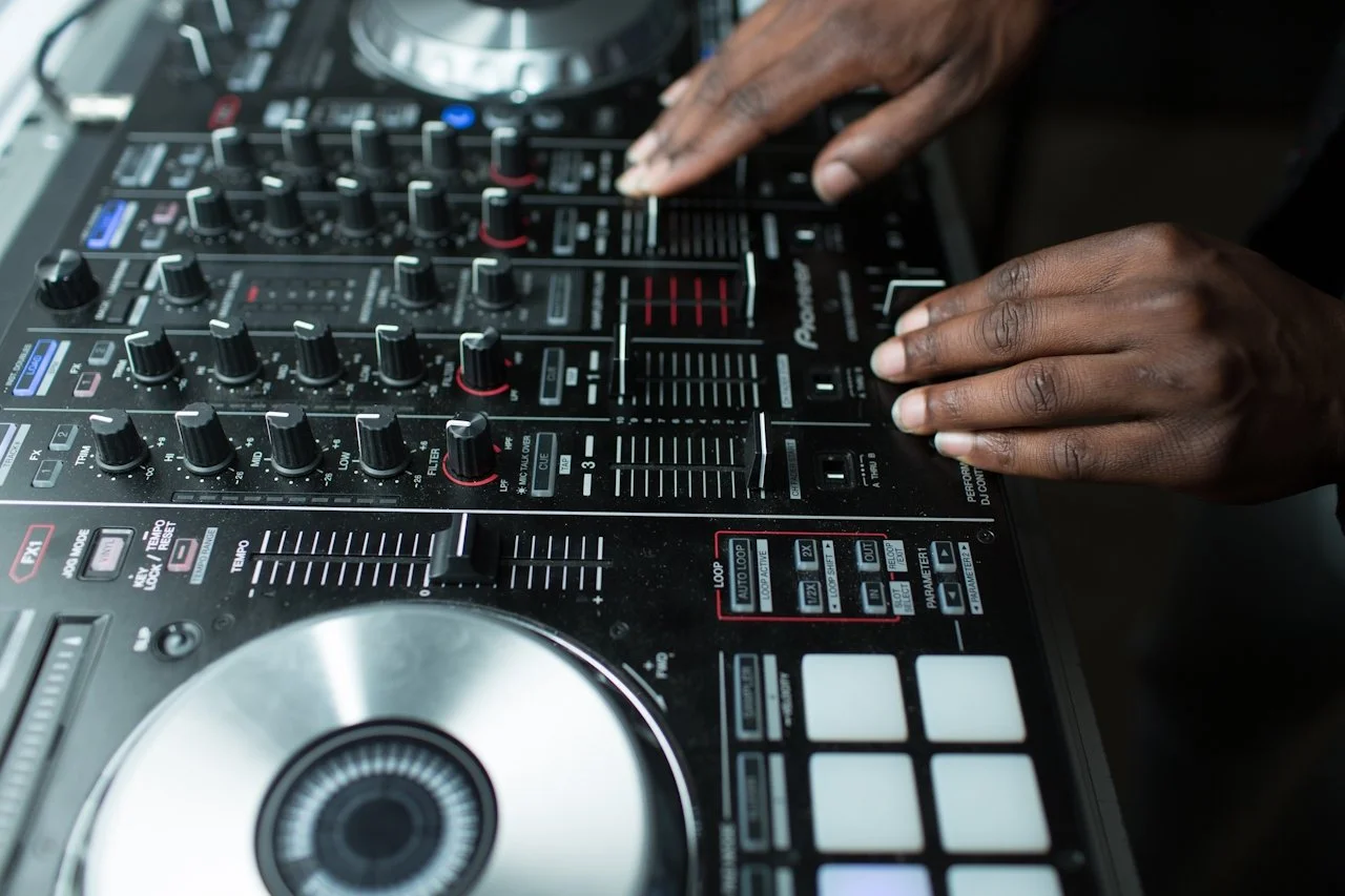 Close-up of a DJ's hands adjusting controls on a professional-grade DJ mixer with various knobs, sliders, and LED indicators.