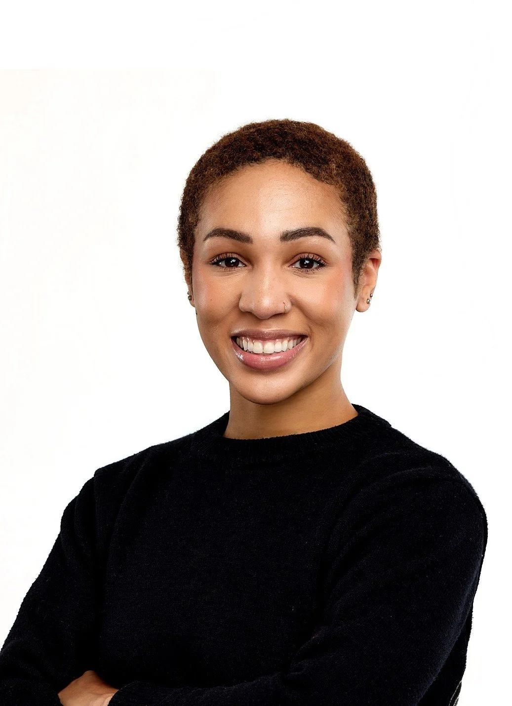 A young woman with short, curly hair smiling, wearing a black sweater, against a plain white background.