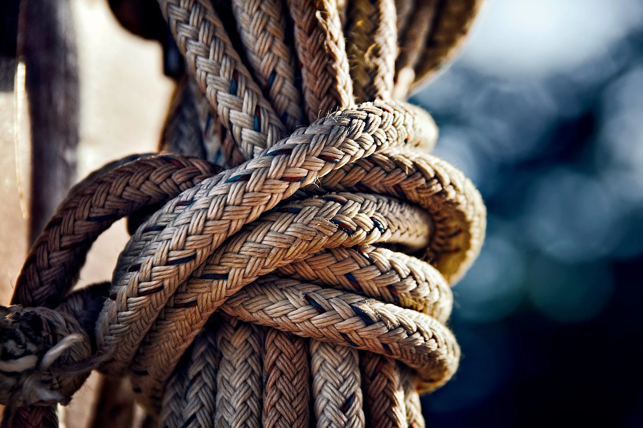 Close-up of beige, dirty rope tied in a knot on a boat with a blurred blue and white background.
