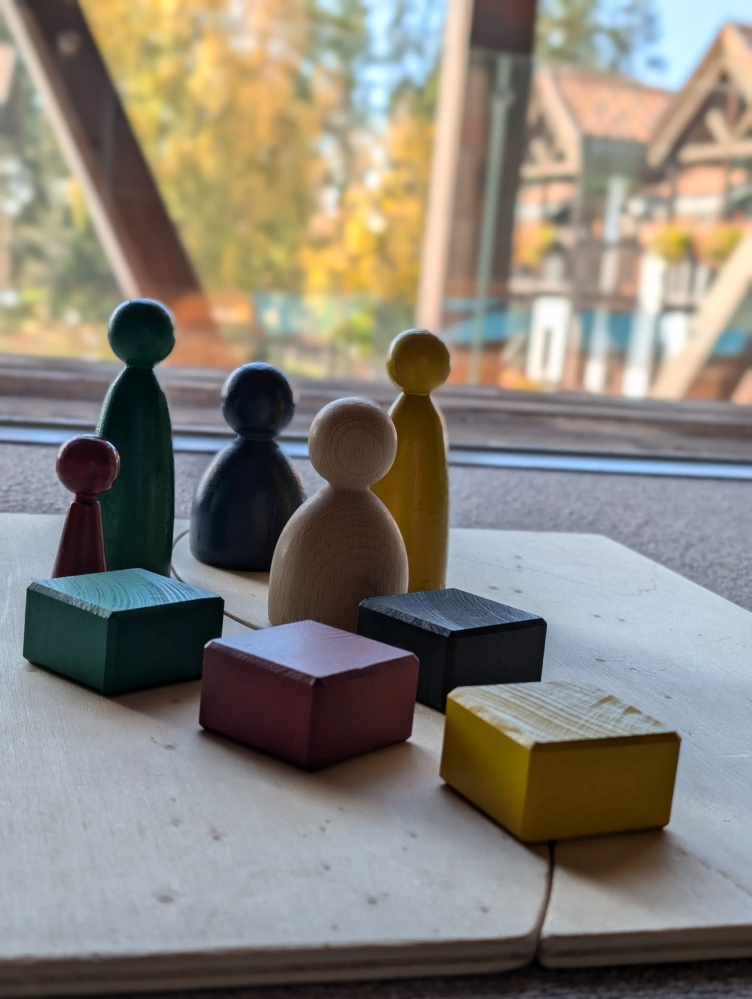 Colorful wooden toys on a table near a window with a blurred view of trees and rooftops outside.