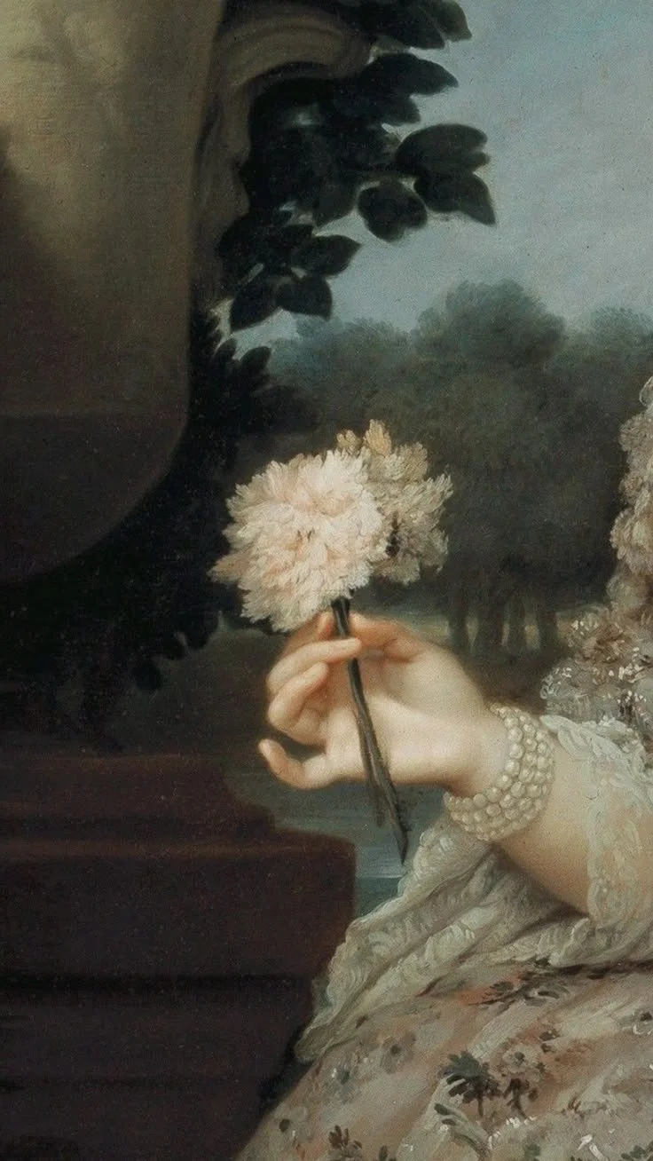 A hand holding a pink flower with a dark stem, wearing a pearl bracelet, in front of a painted landscape scene with trees and cloudy sky.