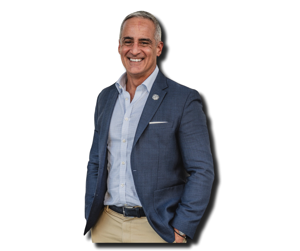 Smiling middle-aged man in a blue blazer, light blue shirt, and beige pants posing with one hand in pocket, against a black background.