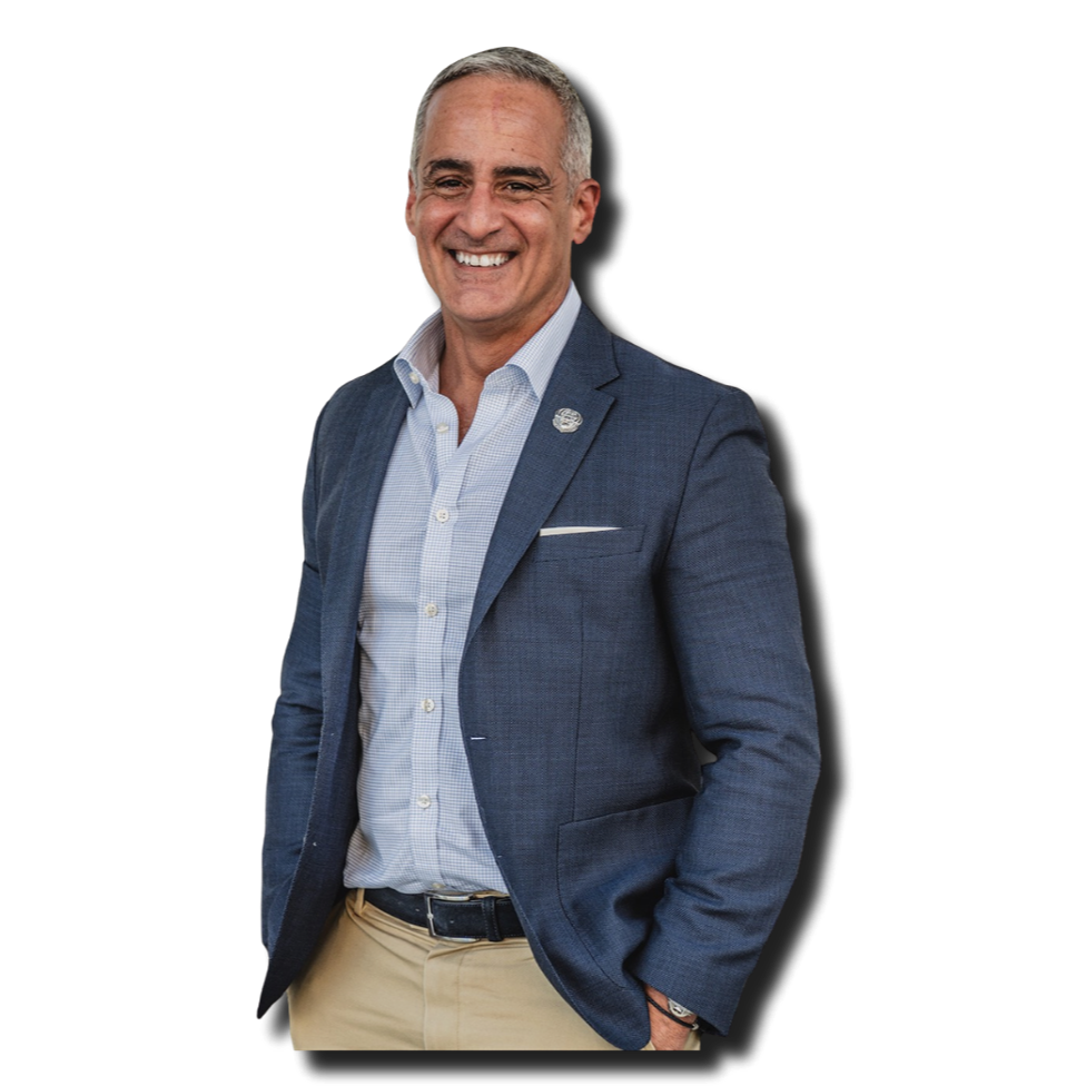 A middle-aged man with gray hair and a bright smile, wearing a blue blazer, light blue dress shirt, and khaki pants, standing against a black background.
