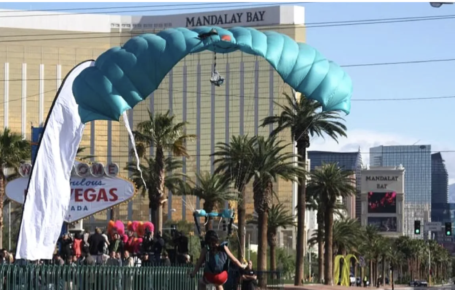 A person with a backpack preparing to parachute jump on the Las Vegas Strip, with the Mandalay Bay hotel in the background and palm trees lining the street.