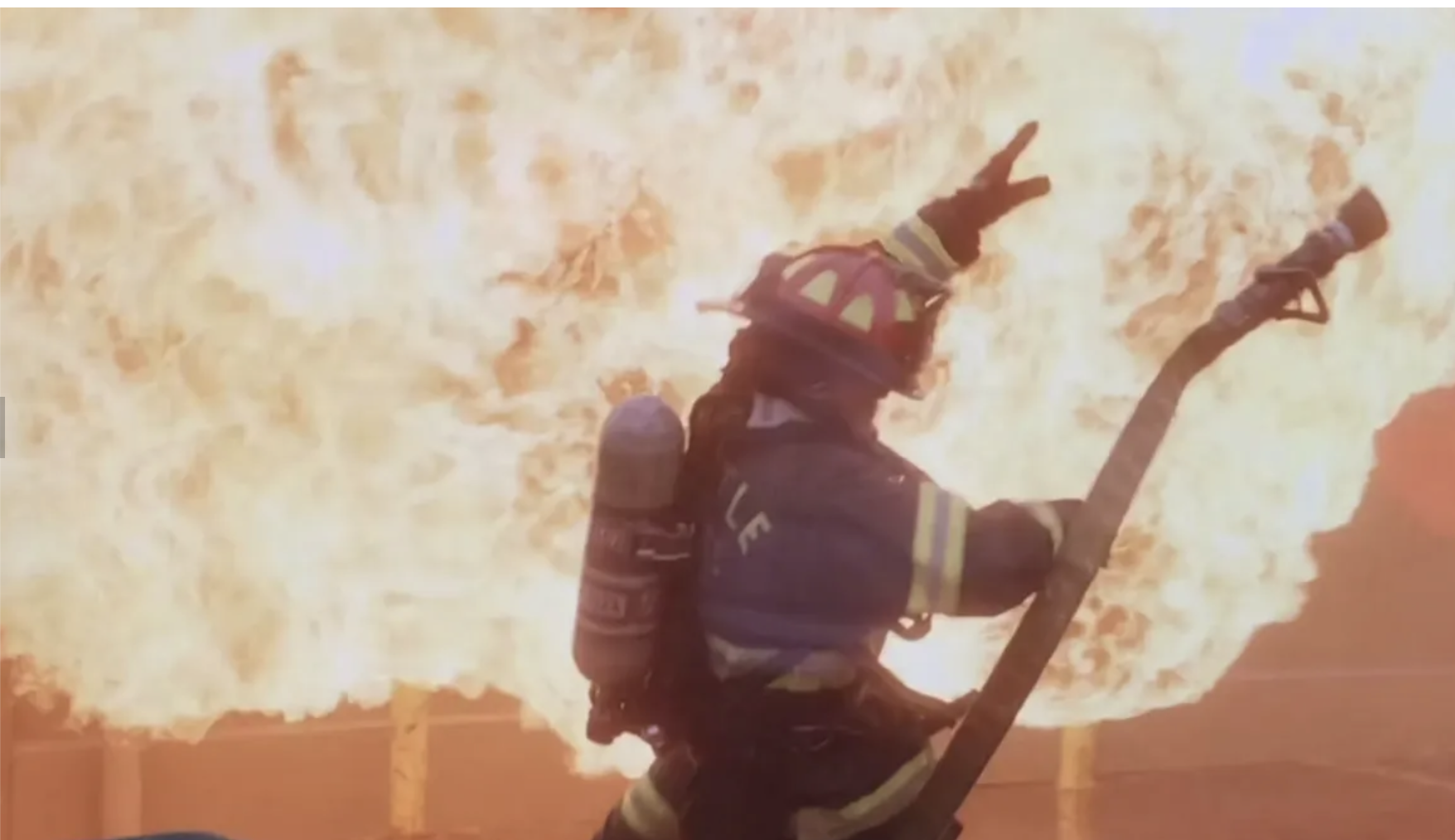 Firefighter holding a tool with flames in the background during a fire rescue operation.