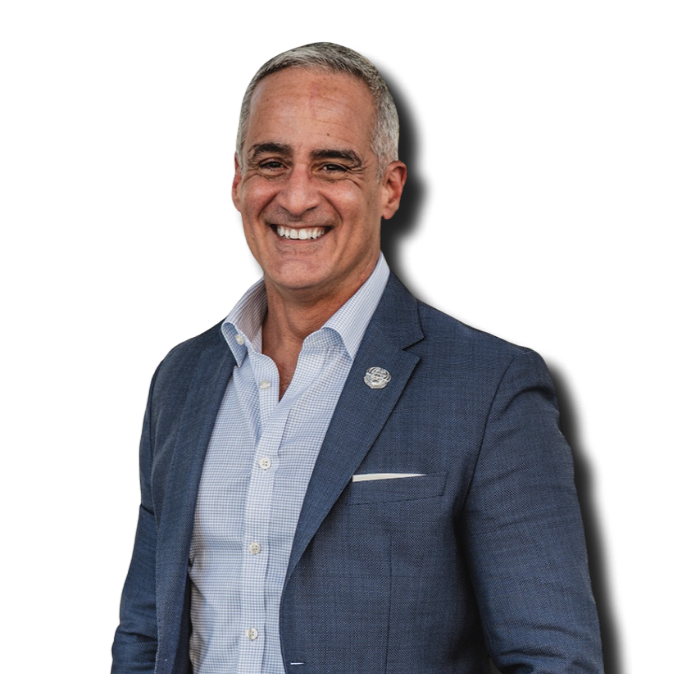 A smiling middle-aged man with gray hair, wearing a blue blazer and light blue shirt, posing in front of a black background.