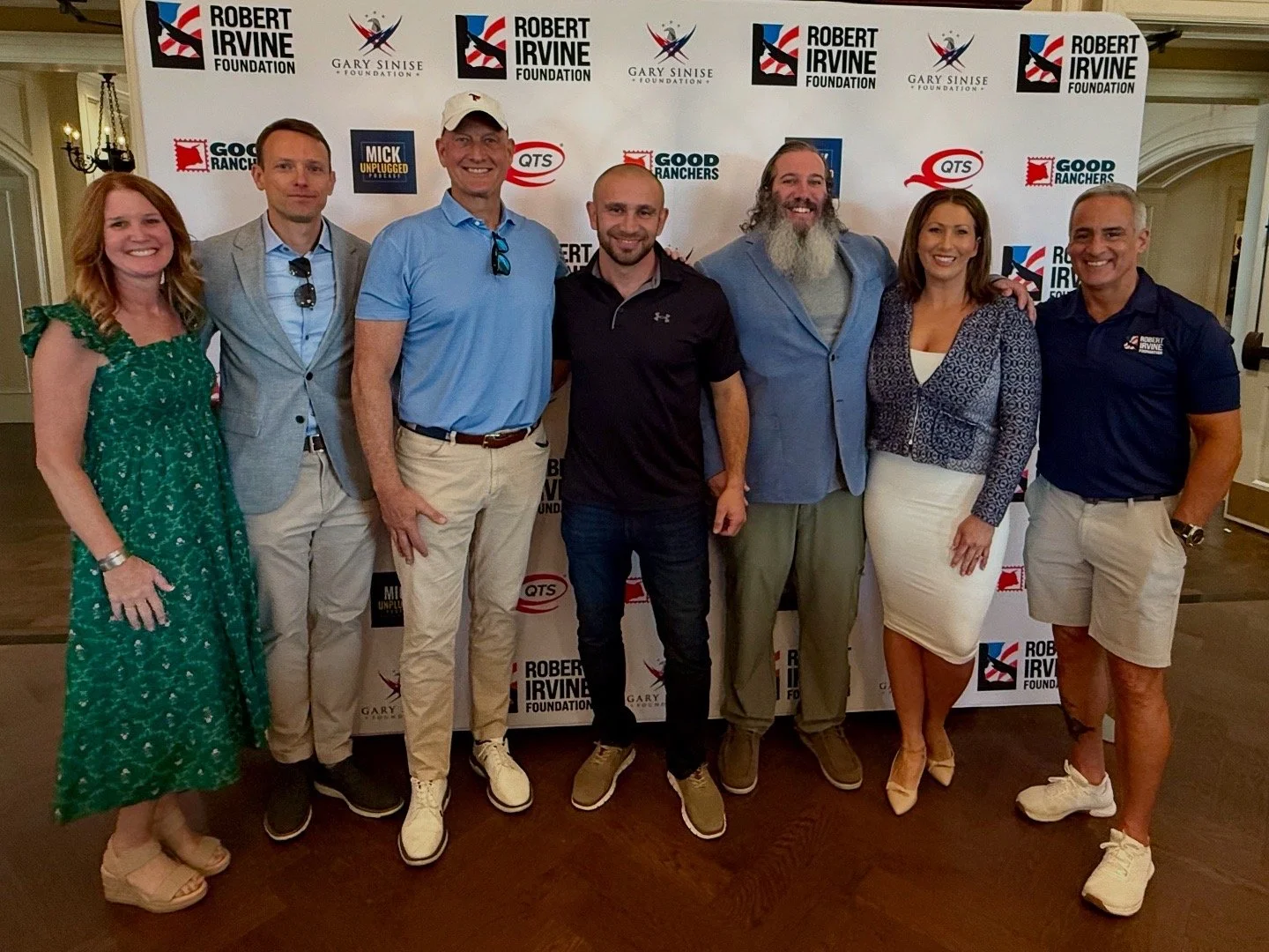 Group of eight people posing indoors in front of a step and repeat banner with logos for the Robert Irvine Foundation and Gary Sinise Foundation.