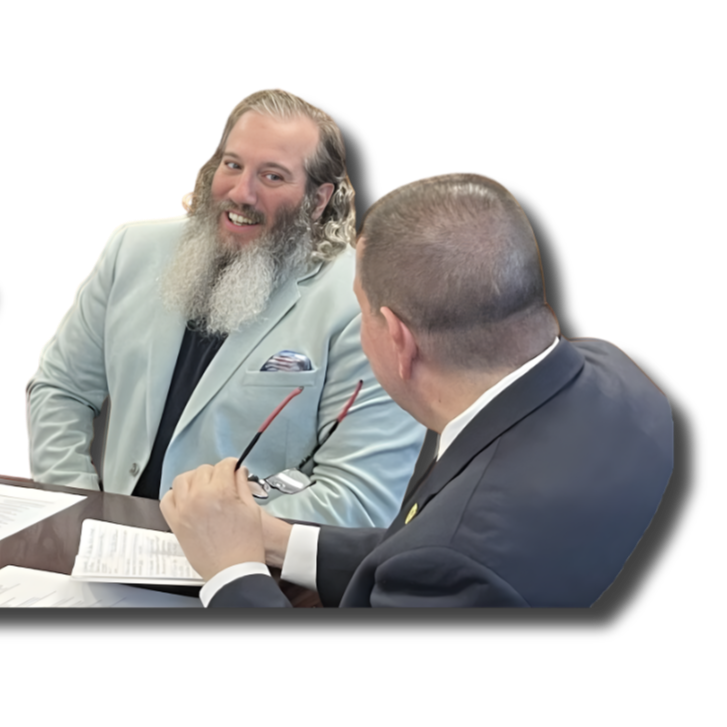 Two men in suits having a conversation at a meeting table, one is holding glasses and smiling.