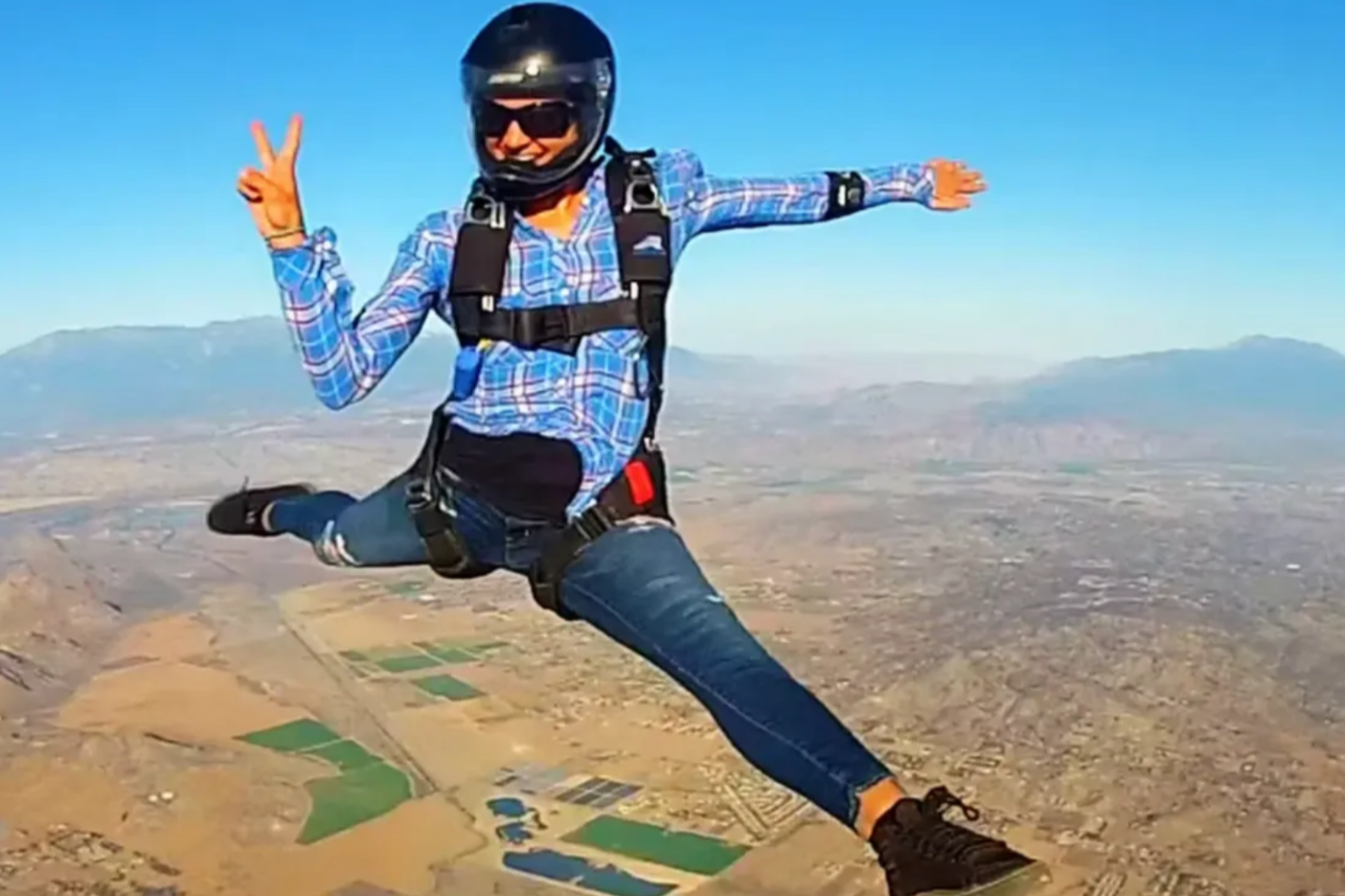 Hannah Betts skydiving wearing a helmet and sunglasses, skydiving with arms and legs spread out over an arid landscape