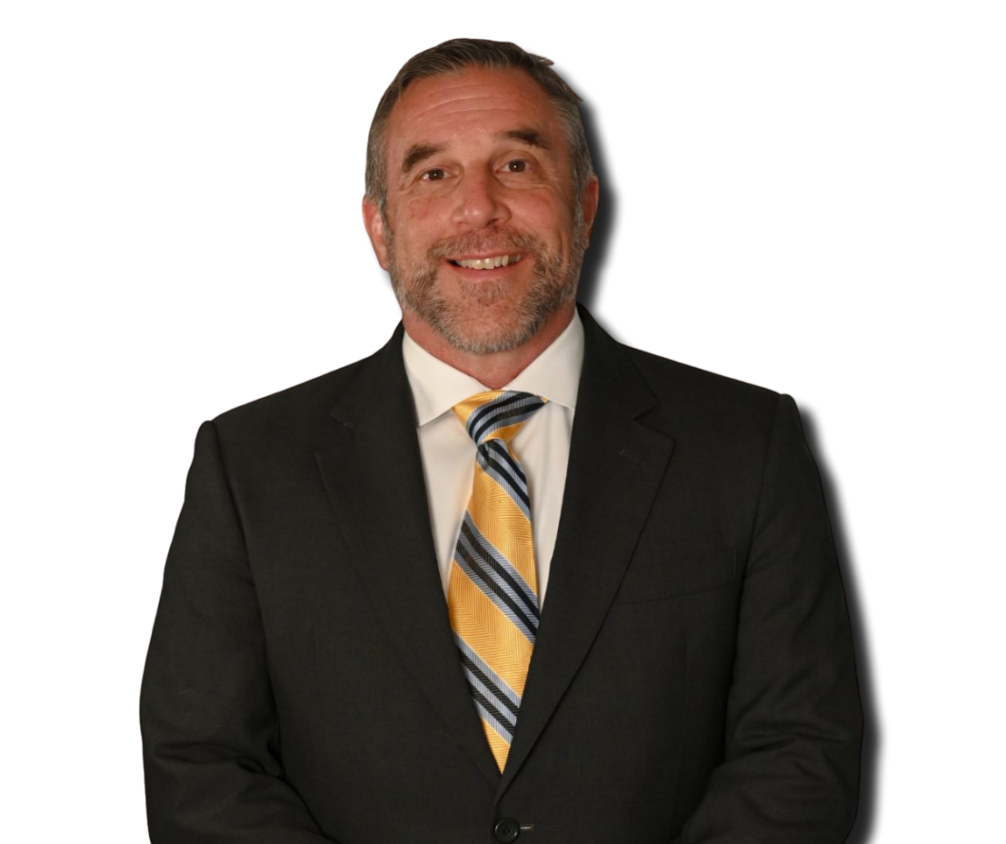 A middle-aged man with gray hair and a beard, wearing a black suit, white shirt, and a striped yellow, black, and white tie, smiling against a black background.