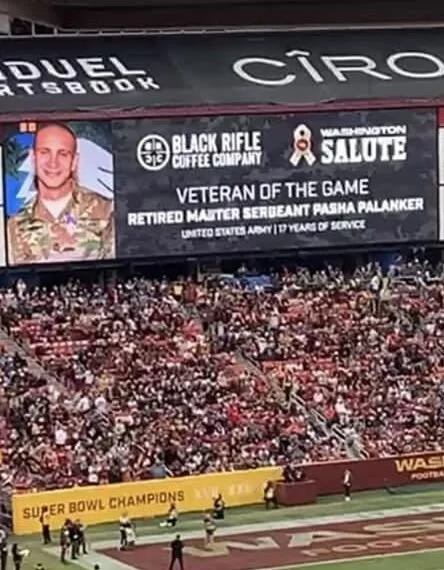 Jumbotron display at a stadium honoring a retired master sergeant, Pasha Palanker, with the Black Rifle Coffee Company logo, Washington Salute emblem, and a photo of the individual in military uniform.