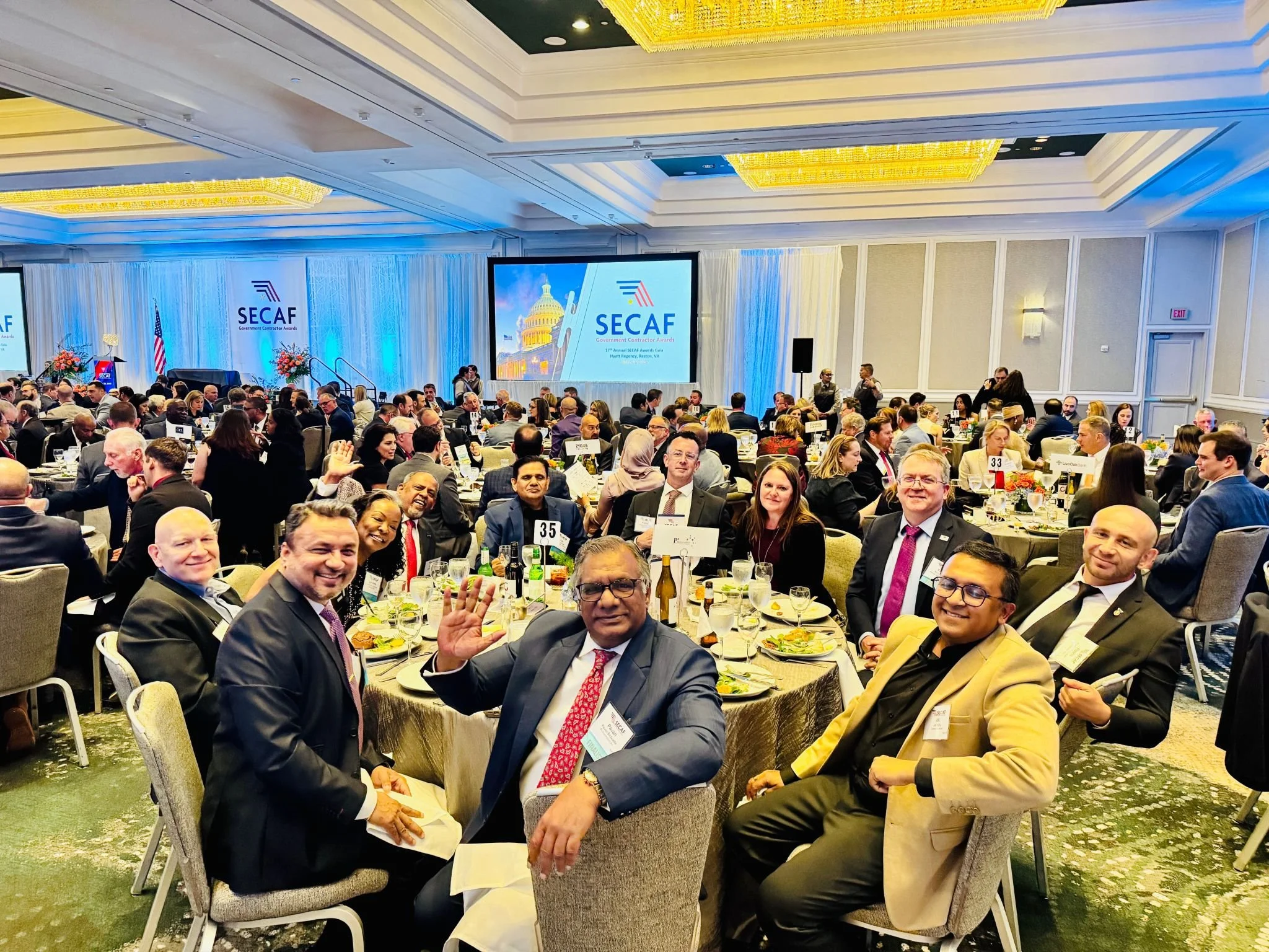 A large group of people at a formal banquet in a decorated conference room, with a stage and large screens displaying 'SECAF' and an image of the Capitol building.