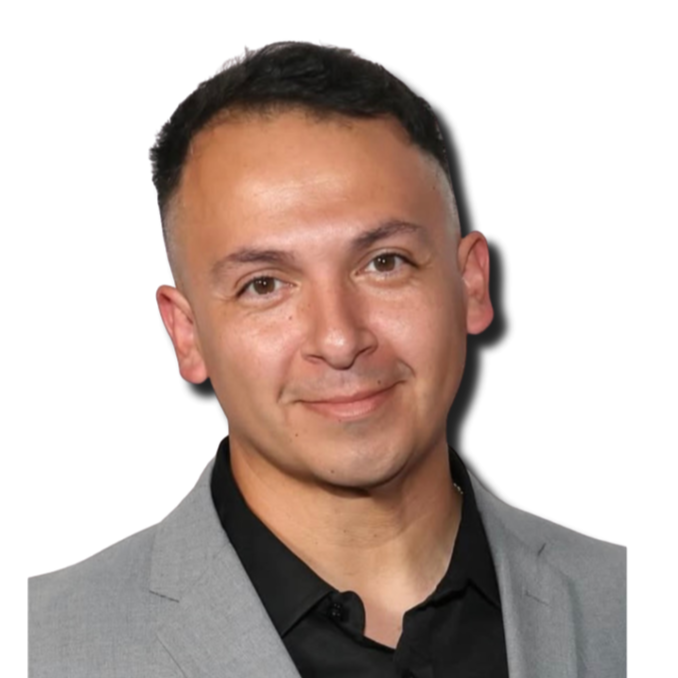 A man with short dark hair, wearing a light gray blazer and black shirt, smiling against a white background.