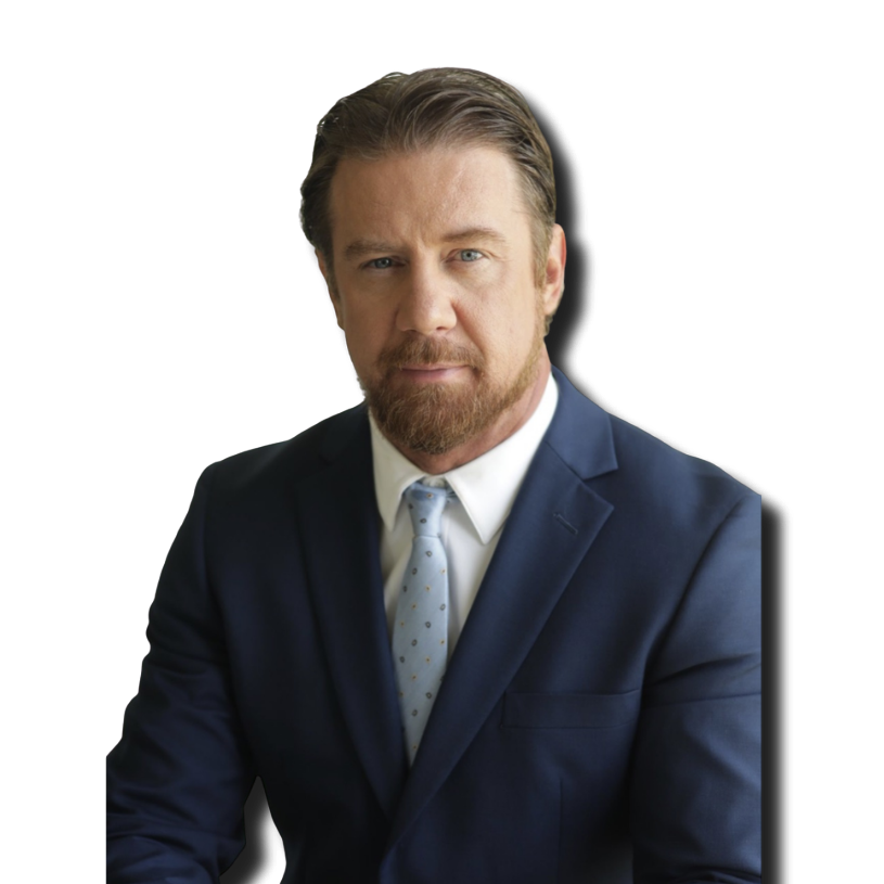 A man with brown hair, a beard, and blue eyes wearing a dark blue suit, white shirt, and light blue tie, looking directly at the camera against a plain black background.