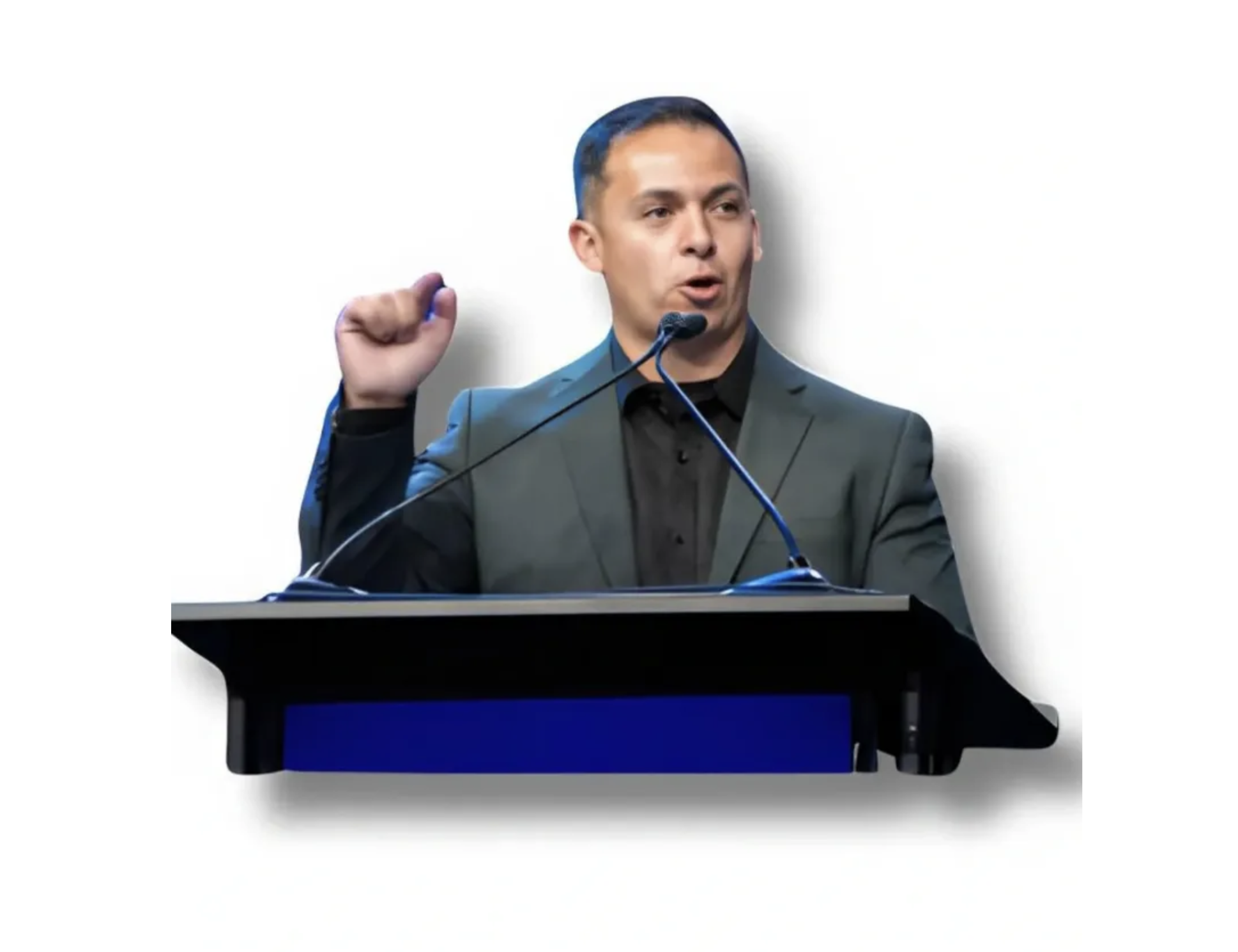 A man in a gray suit and black shirt standing at a podium, speaking into multiple microphones with a plain white background.