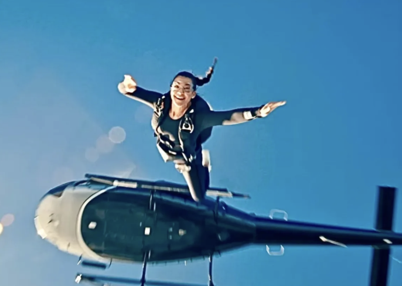 A woman skydiving out of a helicopter, smiling and extending her arms in the sky.