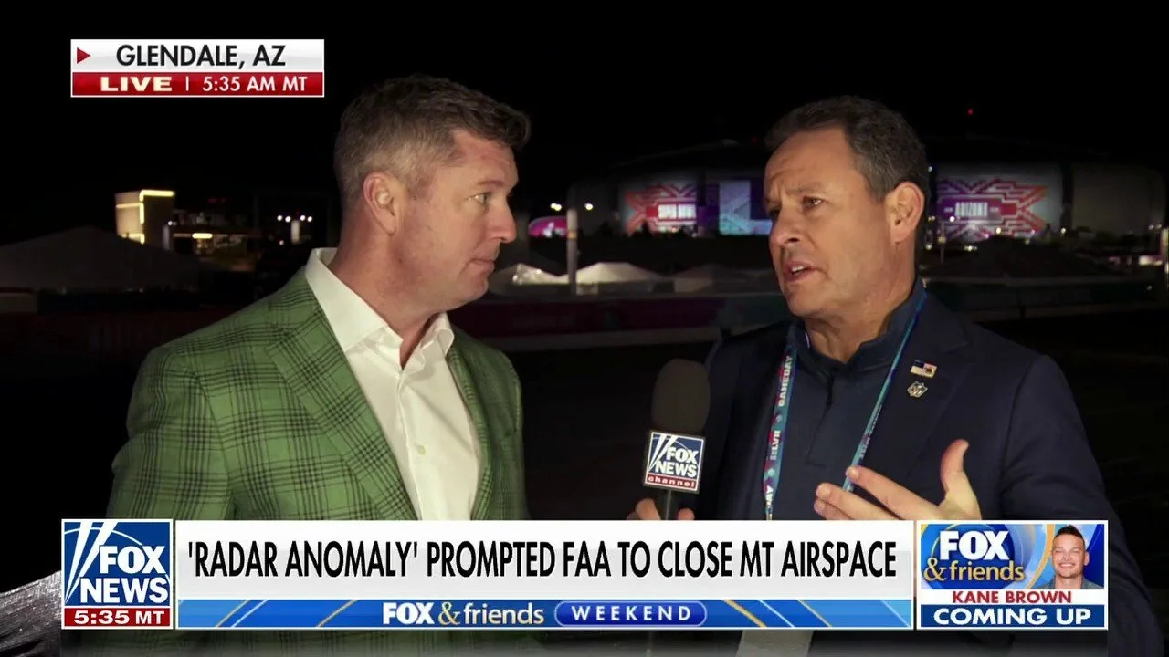 Two men are being interviewed at night in Glendale, Arizona. One man is wearing a green checked blazer, and the other is in a dark suit with a lanyard. The background features illuminated buildings and outdoor lights.