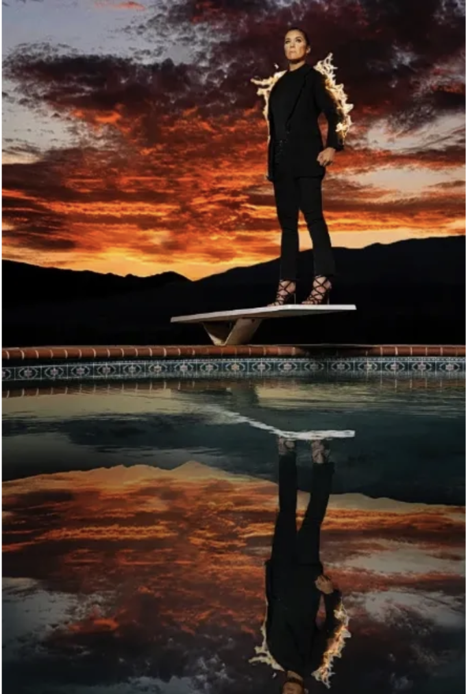 A woman standing on a diving board at sunset, with mountains in the background and a reflection in the pool below.
