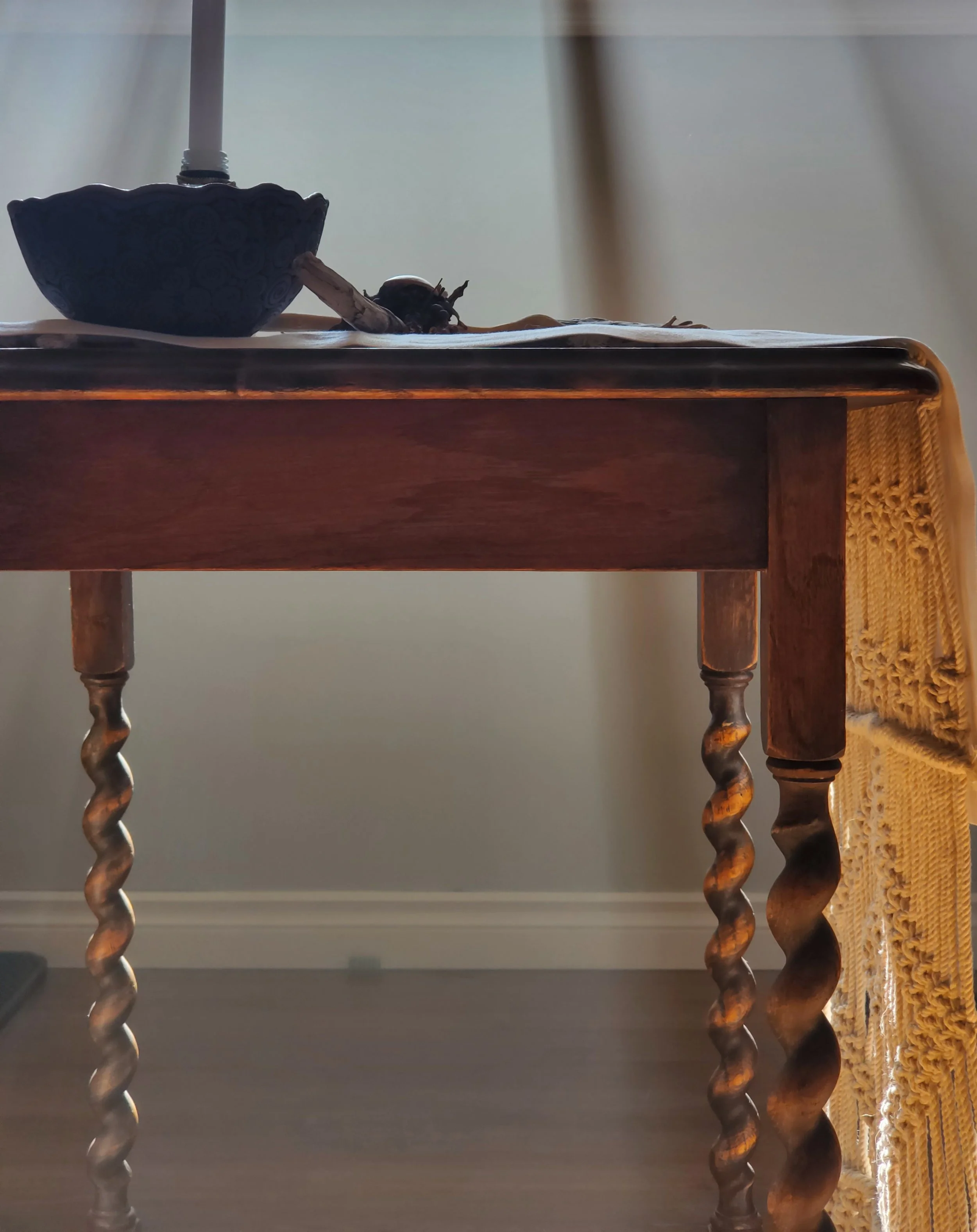 Close-up of a wooden table with twisted, carved legs and a decorative vented yellow fabric draped on the right side.