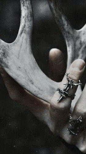 A close-up of a hand wearing unique silver jewelry, holding a deer antler.