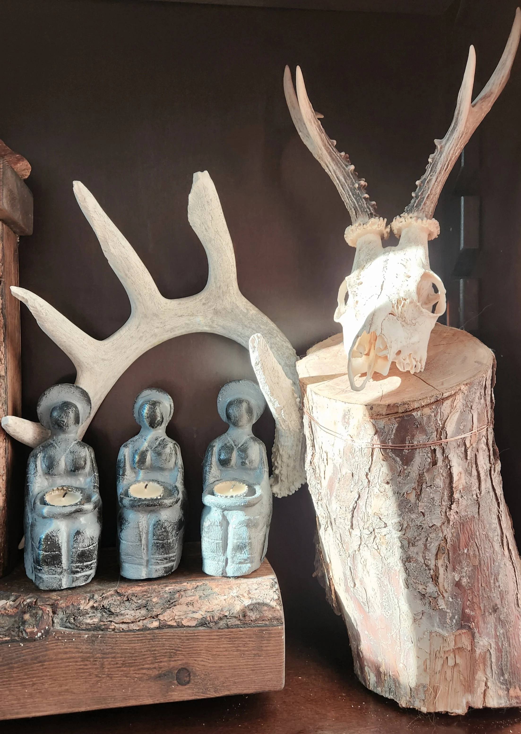Decorative display of wooden and antler sculptures, including three ceramic figures, a large bone or antler piece, and a segment of tree trunk with bark.