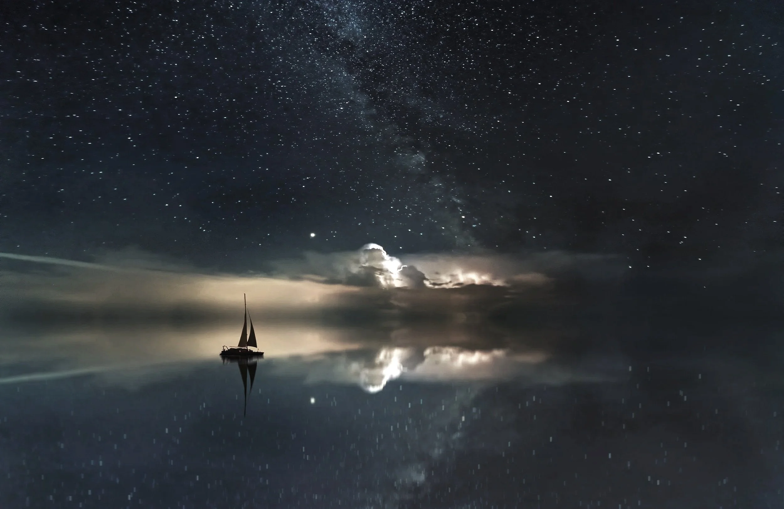 A sailboat floating on calm water at night with a starry sky and the Milky Way galaxy visible above, reflecting on the water.