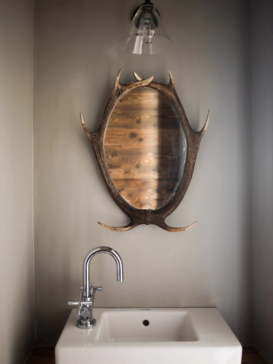 A bathroom wall mirror surrounded by deer antlers above a white sink with a modern chrome faucet.