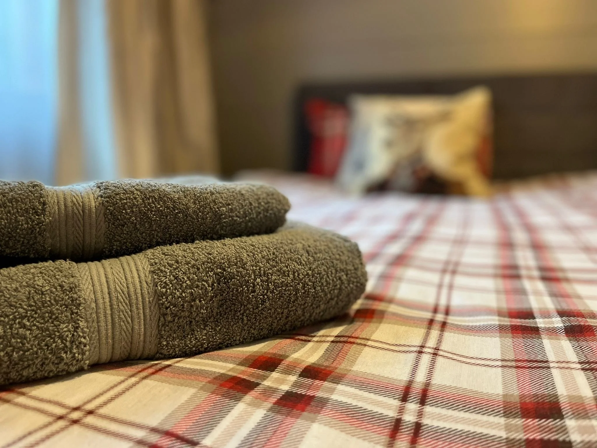 Two towels folded on a bed with a plaid bedspread and a pillow in the background.