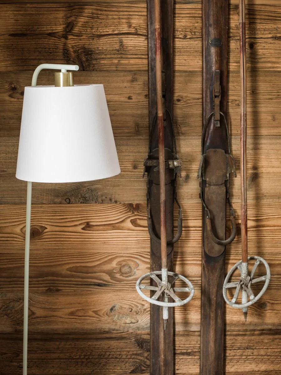 Vintage wooden skis with metal bindings hanging on a wooden wall next to a white lamp.