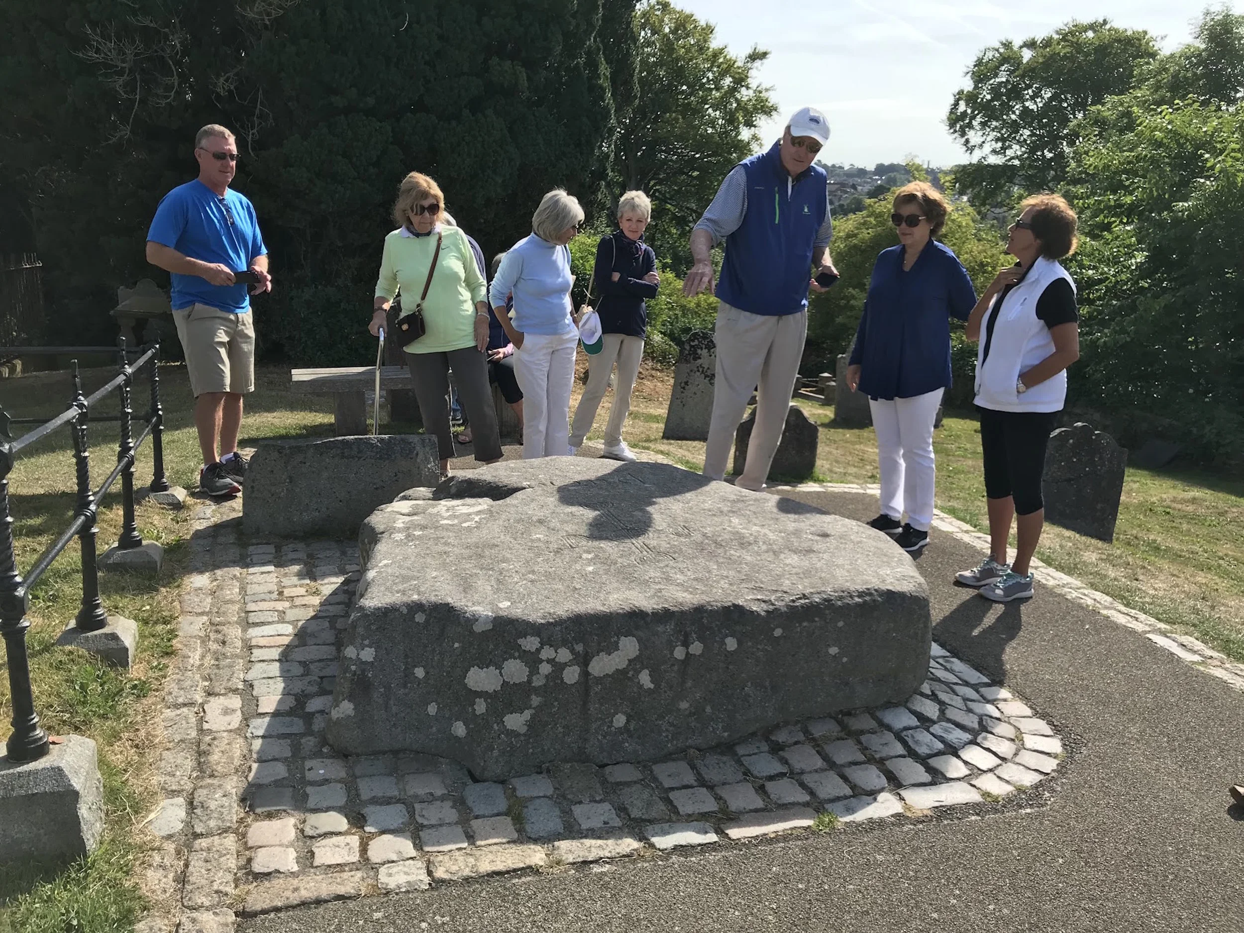 Group of people standing around a large stone, outdoors, sunny day