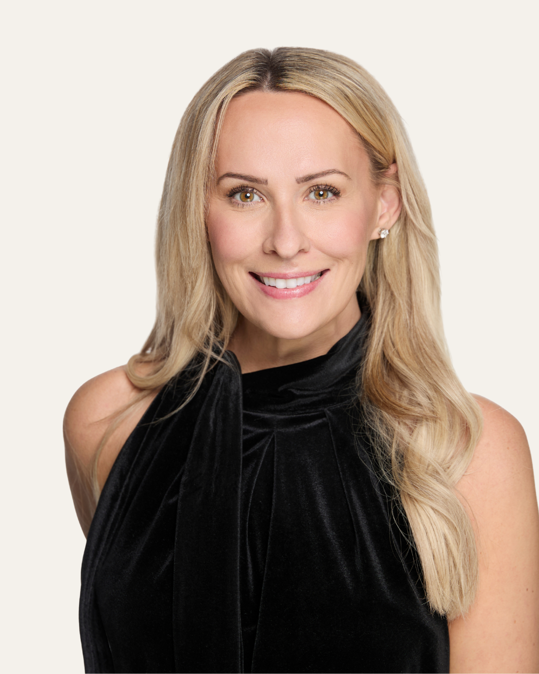 A woman with blonde hair smiling, wearing a black sleeveless top, against a plain light background.