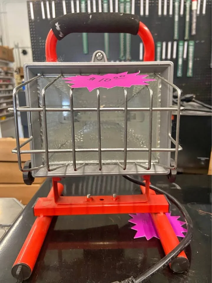 A small metal toaster with a red base and handle, positioned on a black surface, with a pink sale tag on the top and a pink tag on the base, in a store setting.