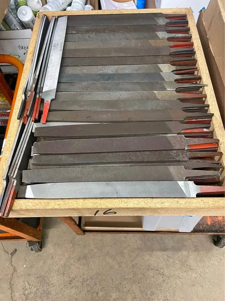 A wooden box filled with various metal hand tools, including several files and rasps, arranged in an organized manner.