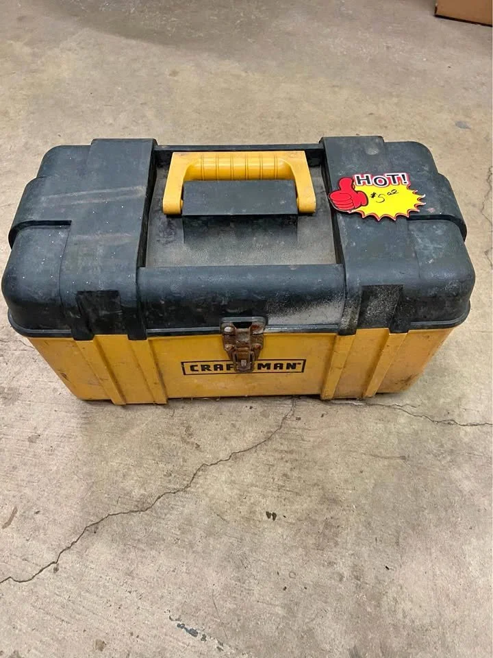 A yellow and black Craftsman toolbox with a handle, placed on a concrete floor. A sticker with a thumbs-up and the word 'HOT!' is attached to the toolbox.