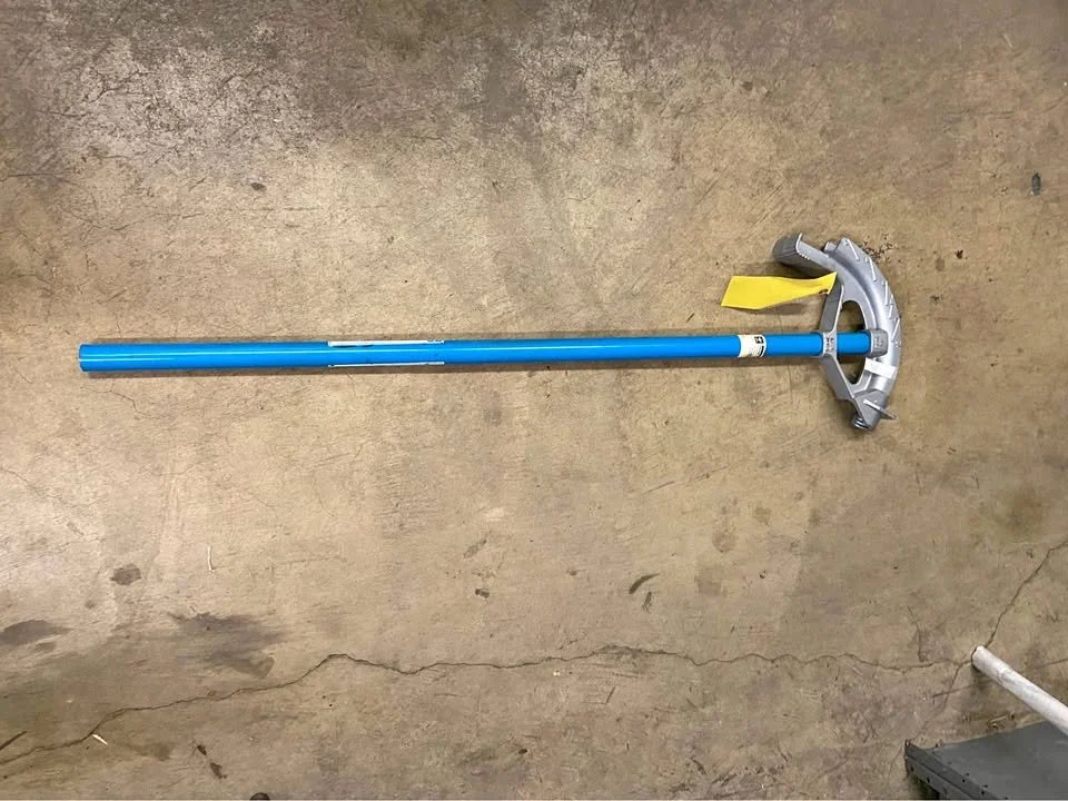 A pool cleaning pole with a telescoping blue handle and a yellow cleaning attachment on a concrete floor.