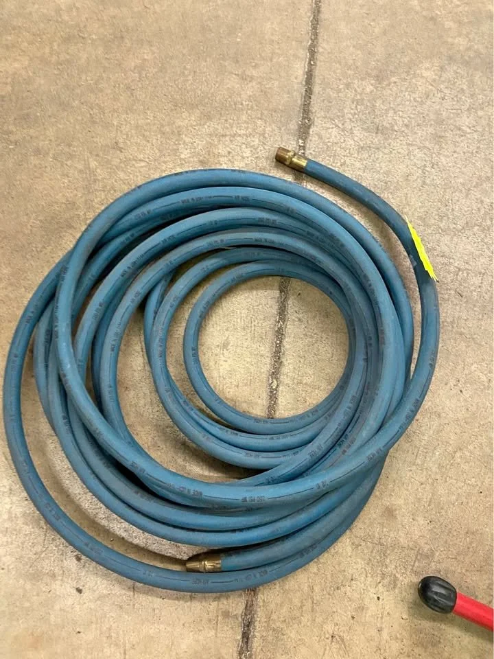 Coiled blue garden hose on concrete floor, with a brass fitting at one end and part of a red and black tool visible at the bottom right.