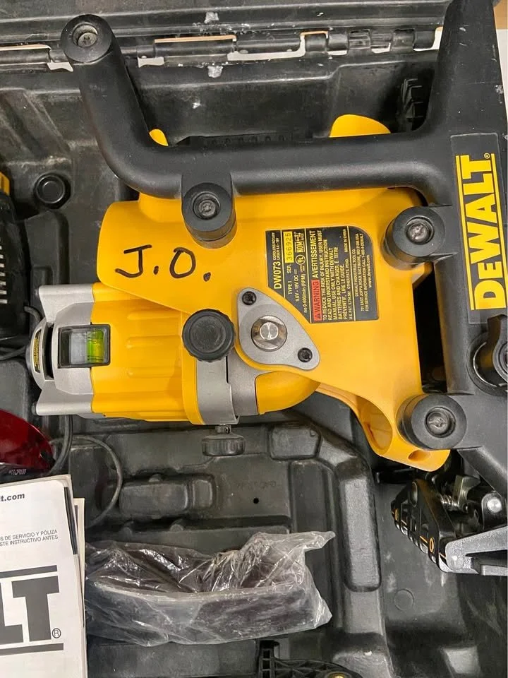 A DeWalt cordless planer placed in a toolbox with a bubble level attached, with handwritten initials J.O on the yellow body.