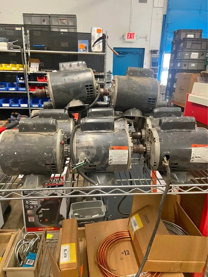 Multiple used electric motors on a metal storage rack in an industrial setting.