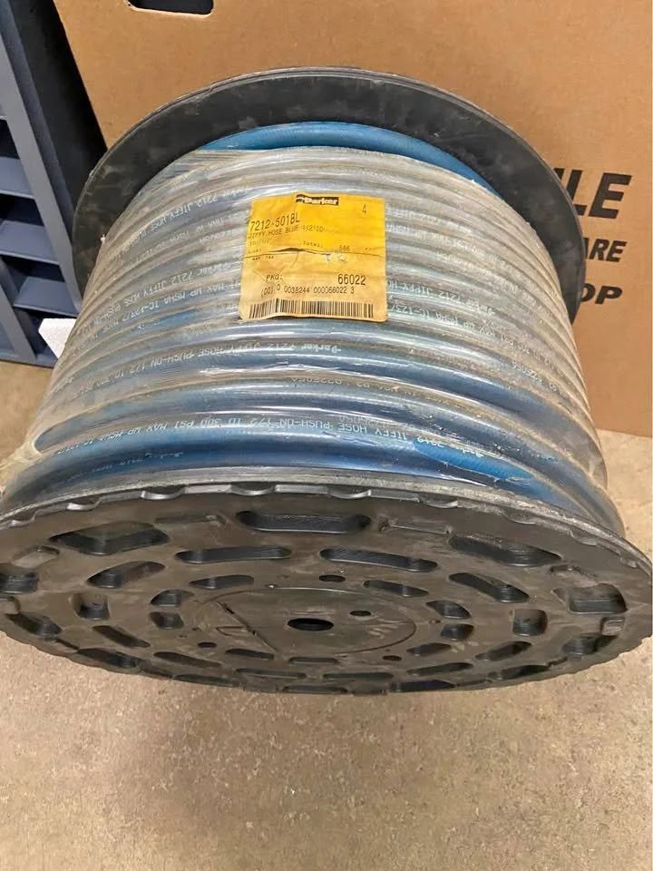 A large spool of high-pressure hydraulic hose with a yellow label attached, resting on a concrete floor in a warehouse or hardware store.