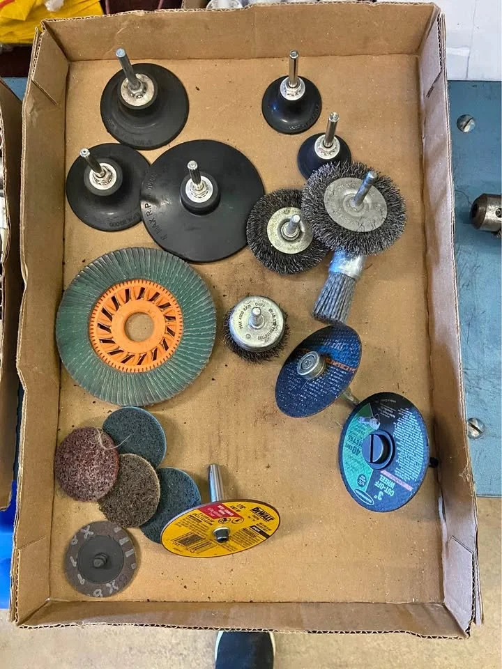 A cardboard box filled with various grinding and polishing tool attachments, including flap discs, grinding wheels, wire brushes, and cutting discs.