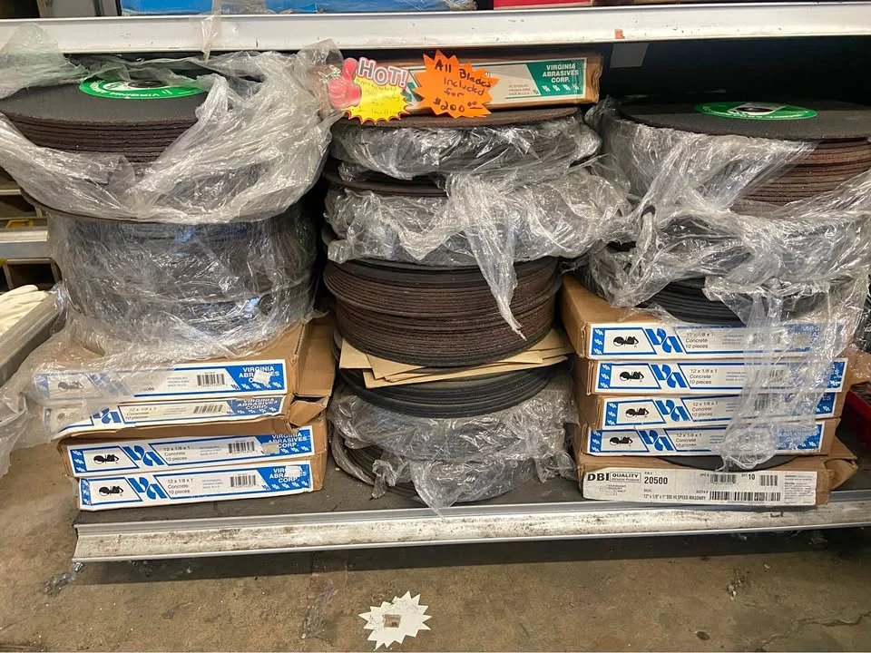 Stacks of circular black and brown rubber mats wrapped in plastic, stored on a metal shelf with boxes labeled 'concrete' on the bottom shelf.