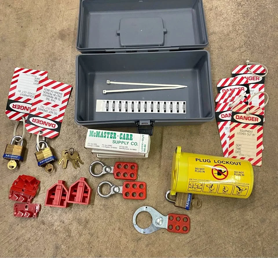Electrical safety lockout/tagout equipment including tags, padlocks, keys, lockout devices, and a lockout hasp, displayed on a surface with an open plastic case.
