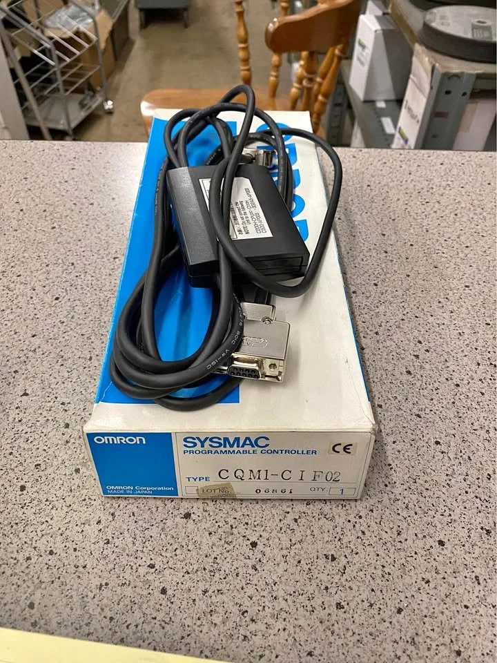 A programmable controller with a black power supply and a thick black cable on top of a blue and white Omron Sysmac box, placed on a gray speckled countertop in a store.
