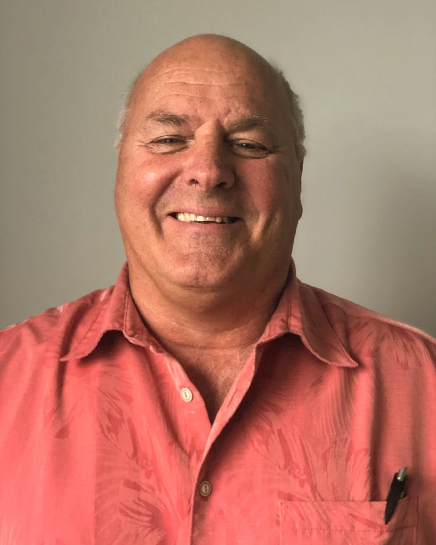 Ron, owner of Mikron Fasteners, standing and smiling in a coral shirt against a light-colored background
