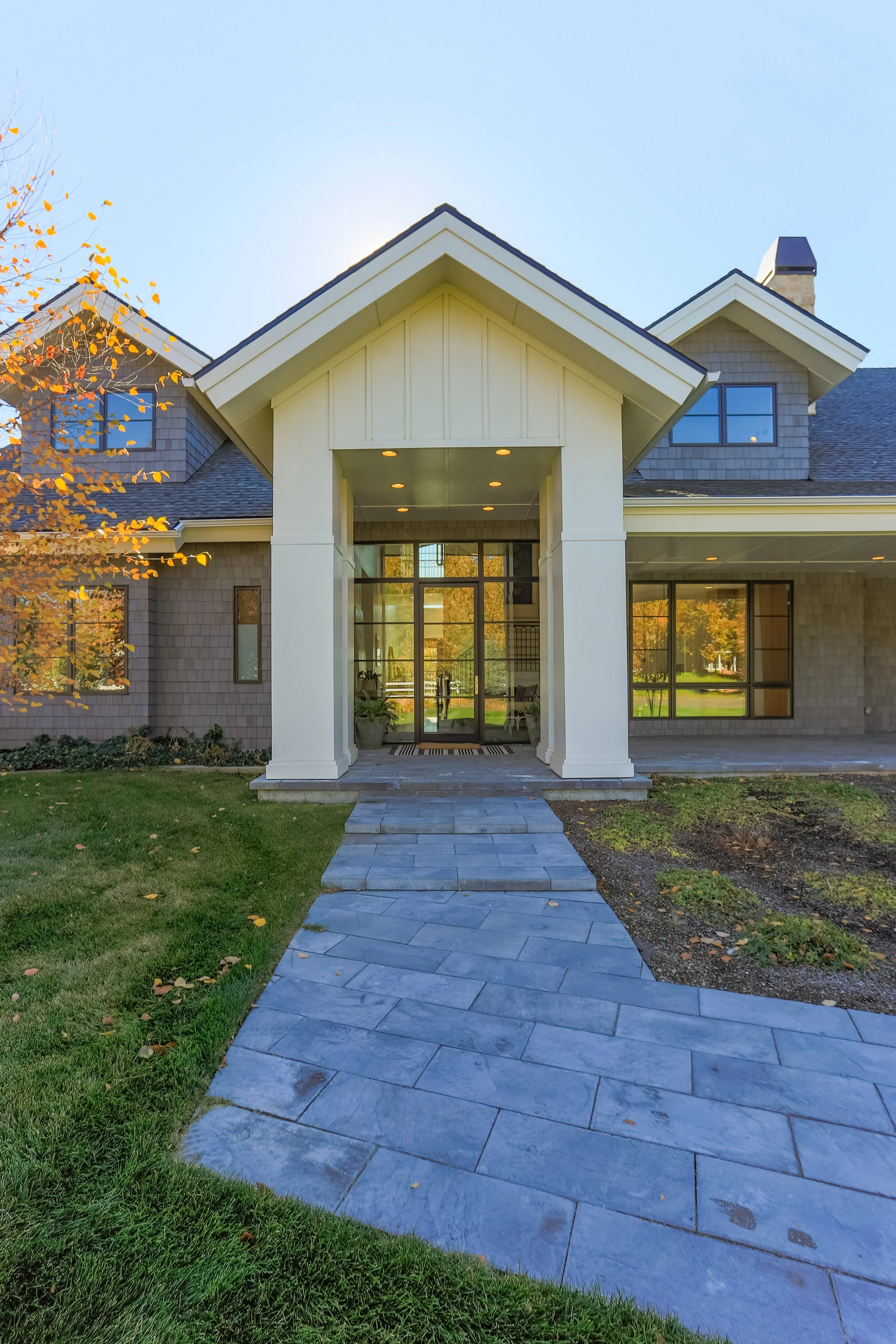 Front view of a modern house with a stone pathway leading to the entrance, large windows, and fall foliage to the side.