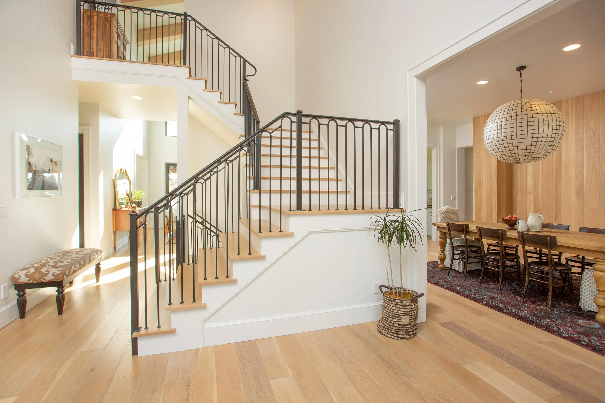 Open living space with staircase, wooden floors, and a dining area with chairs and a table. Features a basket with a plant and hanging paper lantern.