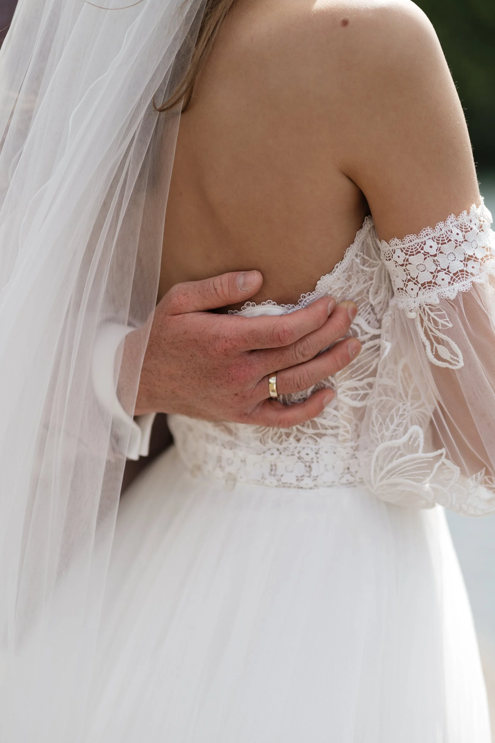 Nahaufnahme einer Frau im weißen Brautkleid mit Spitze, die ein Schleier trägt, bei einer Hochzeit im Freien.